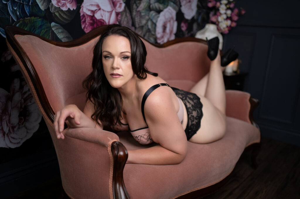 Beautiful brown haired curvy woman on pink couch with floral background for boudoir