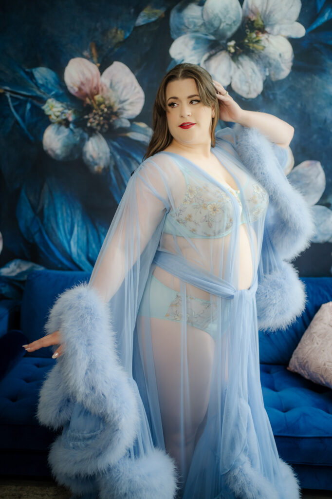 Beautiful curvy woman in blue lingerie and Catherine D'Lish luxury robe, at Georgian Bay Boudoir studios, against a blue floral backdrop
