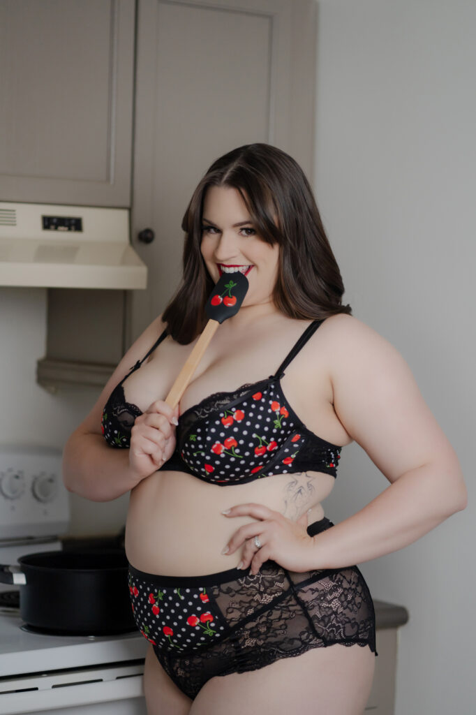 Beautiful curvy woman in black and cherry lingerie, poses in kitchen with pinup boudoir style